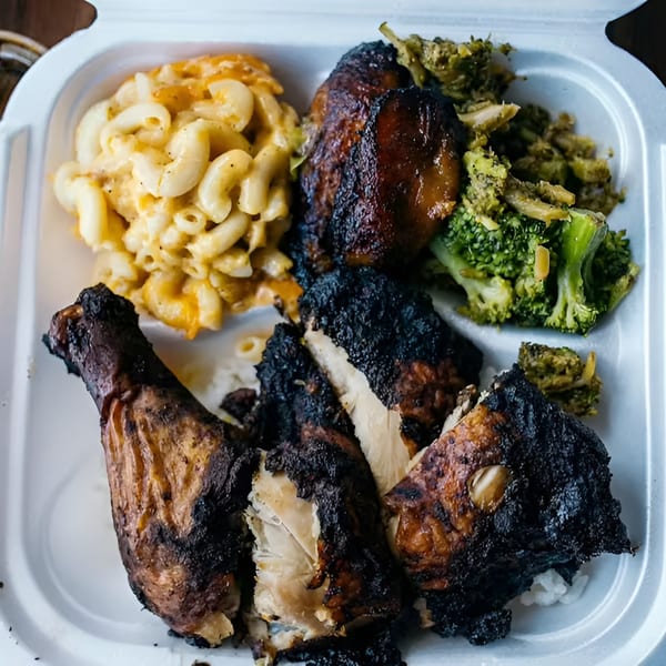 Soul food meal with grilled chicken, macaroni and cheese, and broccoli in a takeout container.