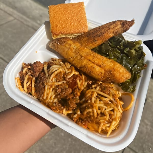 A soul food takeout container with spaghetti, fried fish, collard greens, and cornbread.