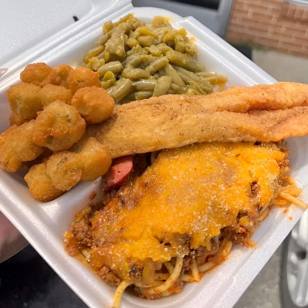 A soul food platter with fried fish, baked spaghetti, fried okra, and green beans in a styrofoam container.